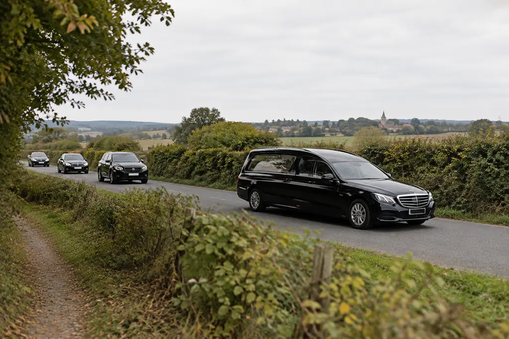 Un corbillard sans marque circule sur une route de campagne suivi de voitures discrètes.