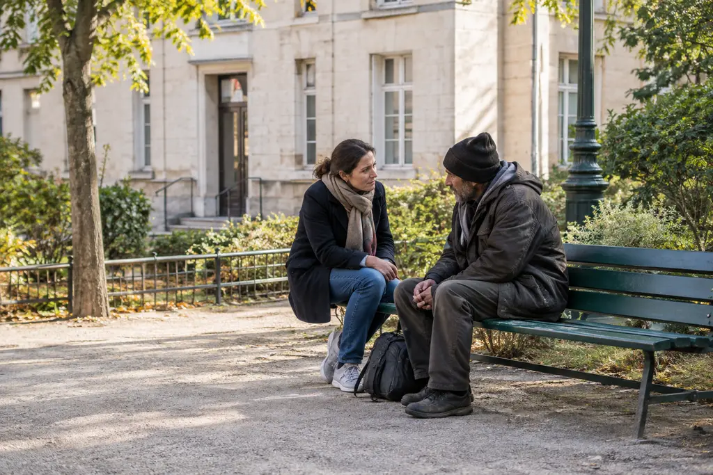 Une travailleuse sociale écoute un homme assis près d’un bâtiment communal et d’un square.